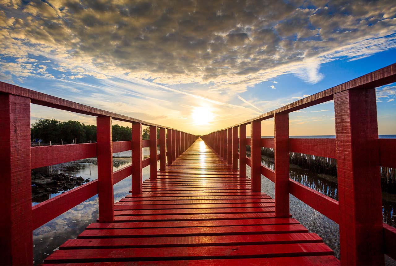 Red bridge over stream leading into the sunset