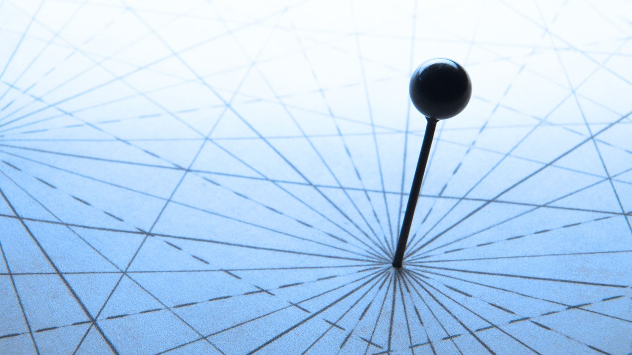 A push pin is positioned in the middle of a compass rose on a map with navigational lines intersecting with the pushpin.