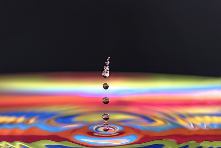 Water drop making ripple on multicolored base and black background